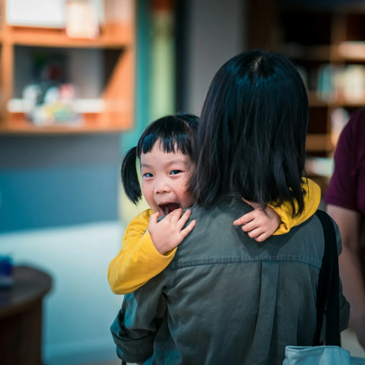 An adult carrying a smiling young child in a warm indoor setting.