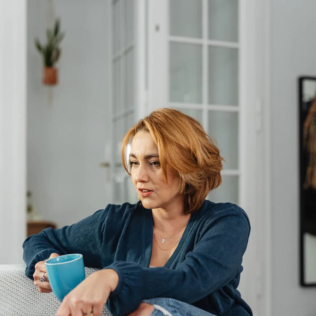 An adult sitting on a sofa with a mug, thinking something over.