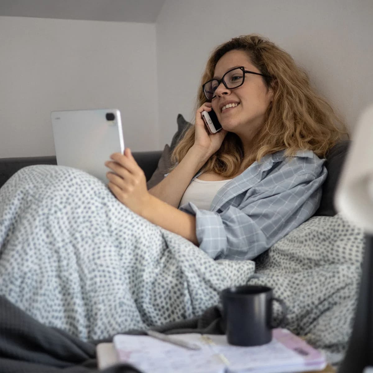 An adult at home on the phone, with a tablet and an open notebook.